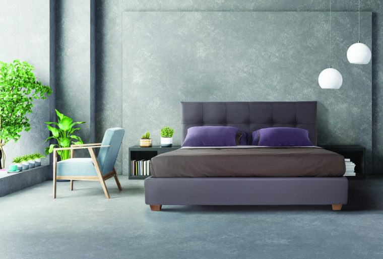 Blue dark armchair near cabinet and bed with sheets in bedroom i